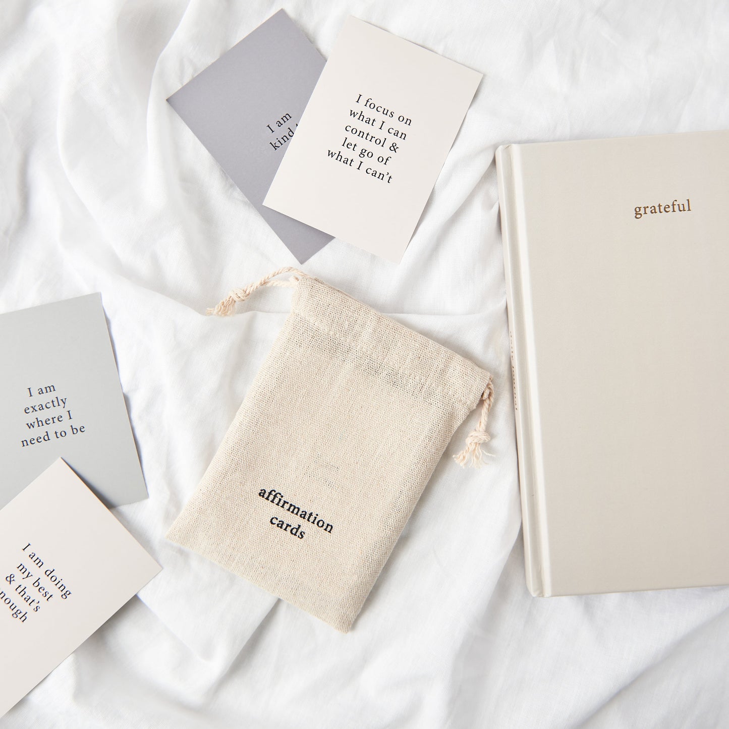 A set of affirmation cards, a bag an gratitude journal sitting on a bed