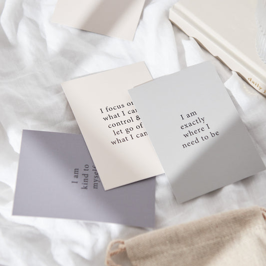 A set of 3 affirmation cards sitting on a bed. Affirmations read: I am kind to myself, I focus on what I can control and let go of what I can't, I am exactly where I need to be 