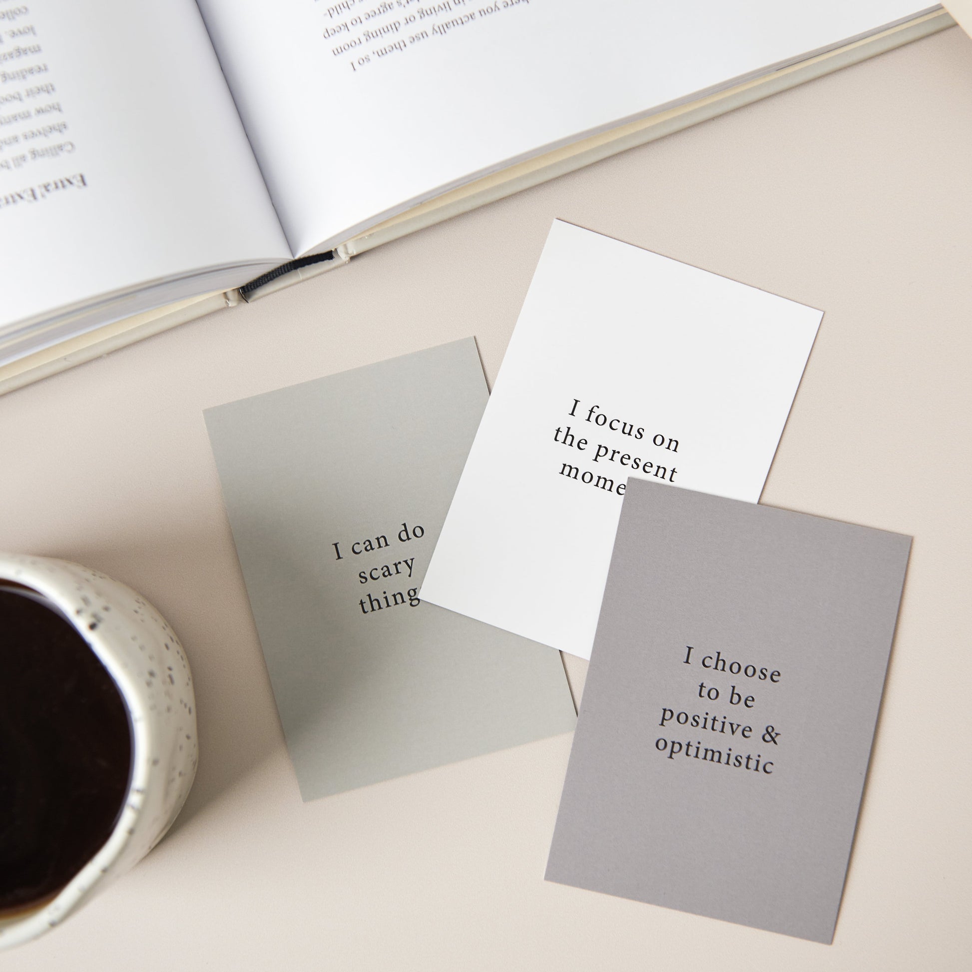 A set of 3 affirmation cards on a table along with a cup of coffee
